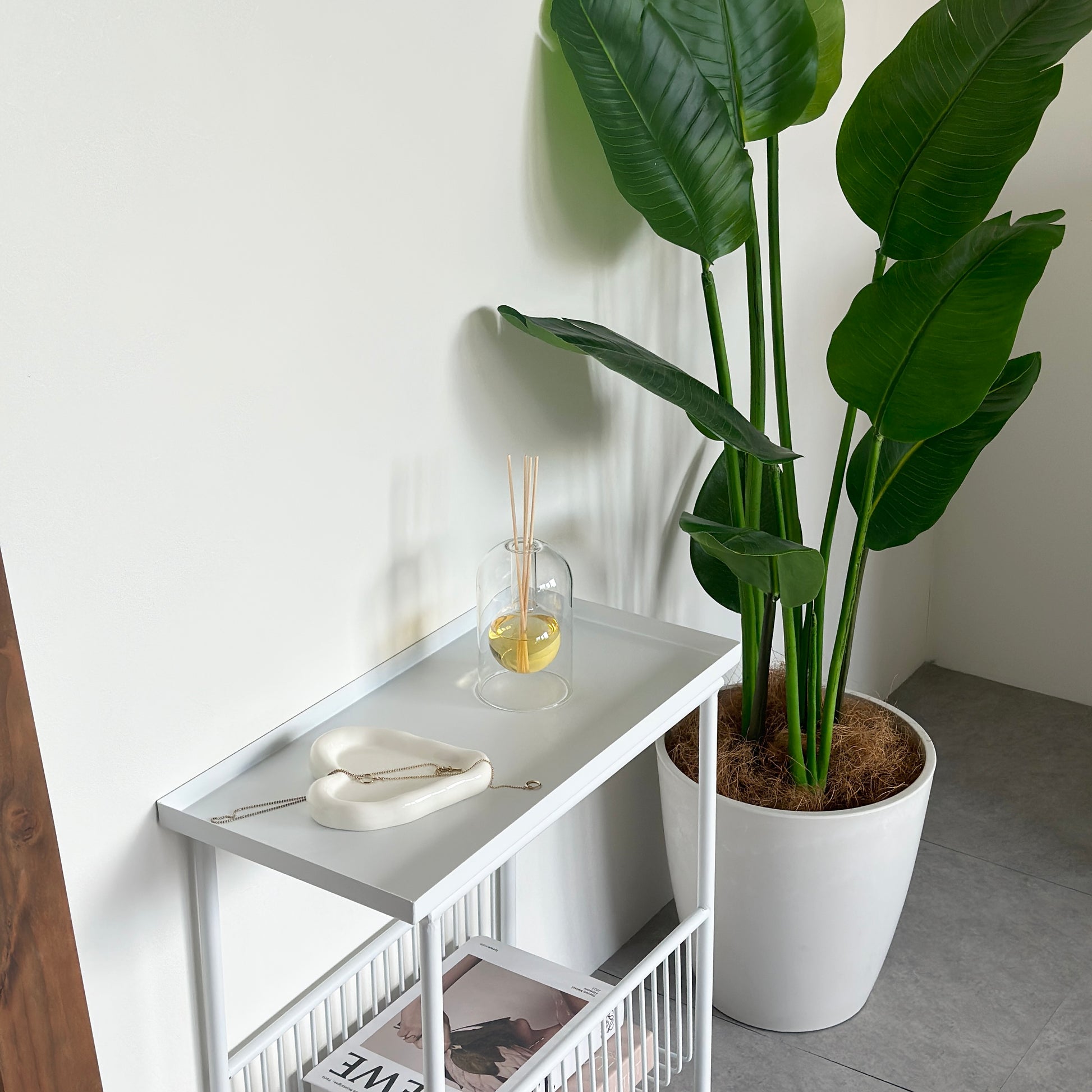 ホワイトのサイドテーブルの上に、ルームフレグランスと縁があるホワイトのハート型のプレートにアクセサリーが乗っている様子