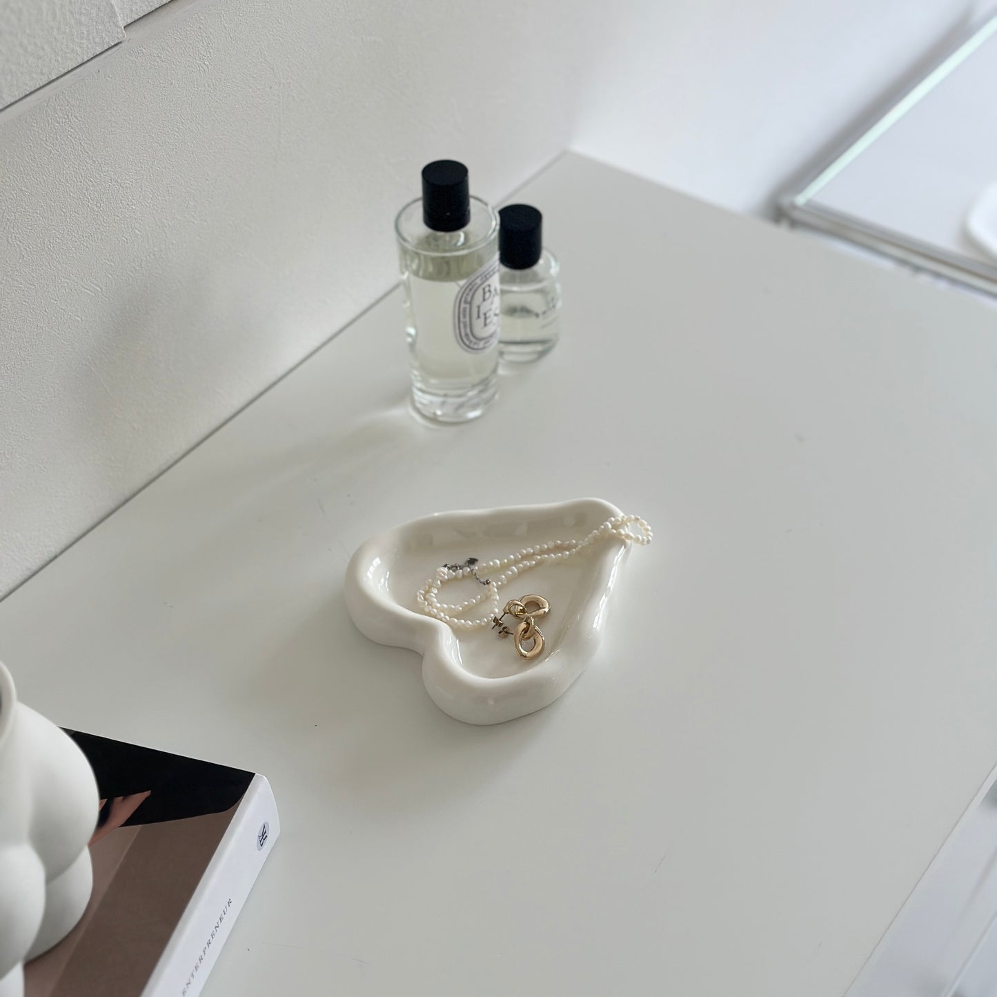 ホワイトのテーブルに置いた縁があるホワイトのハート型のプレートにアクセサリーが乗っている様子