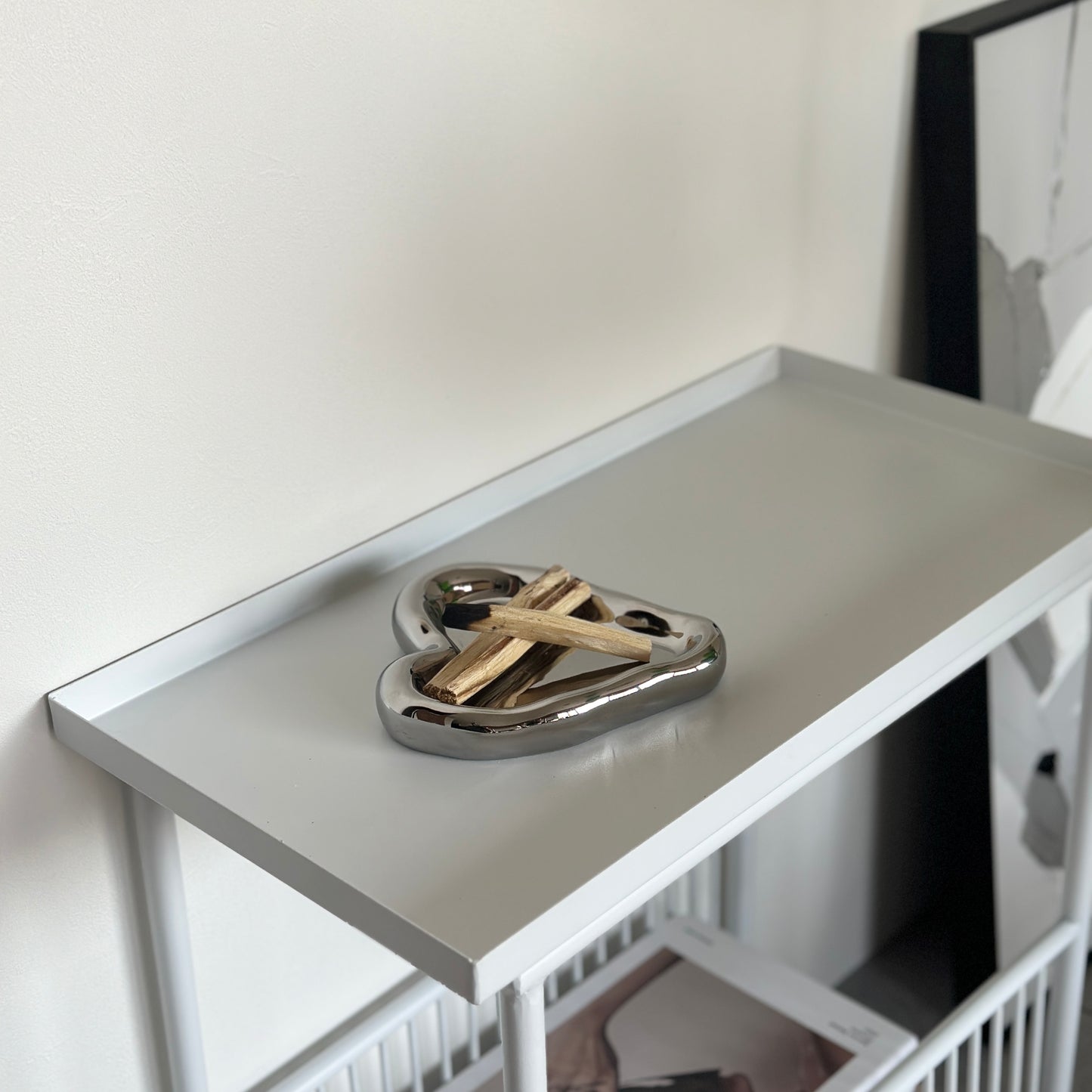 ホワイトのサイドテーブルの上に置いた縁があるシルバーのハート型のプレートにパロサントを乗せている様子