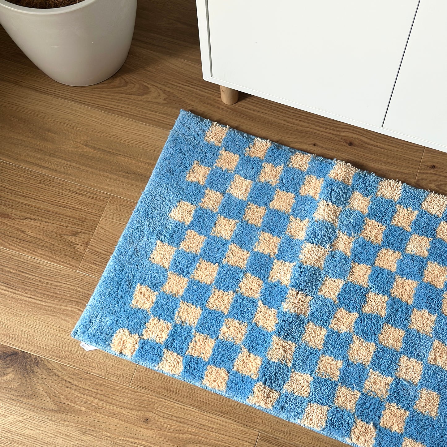 ブルーのグリッドチェック柄のミニラグを白棚の前に敷いている様子