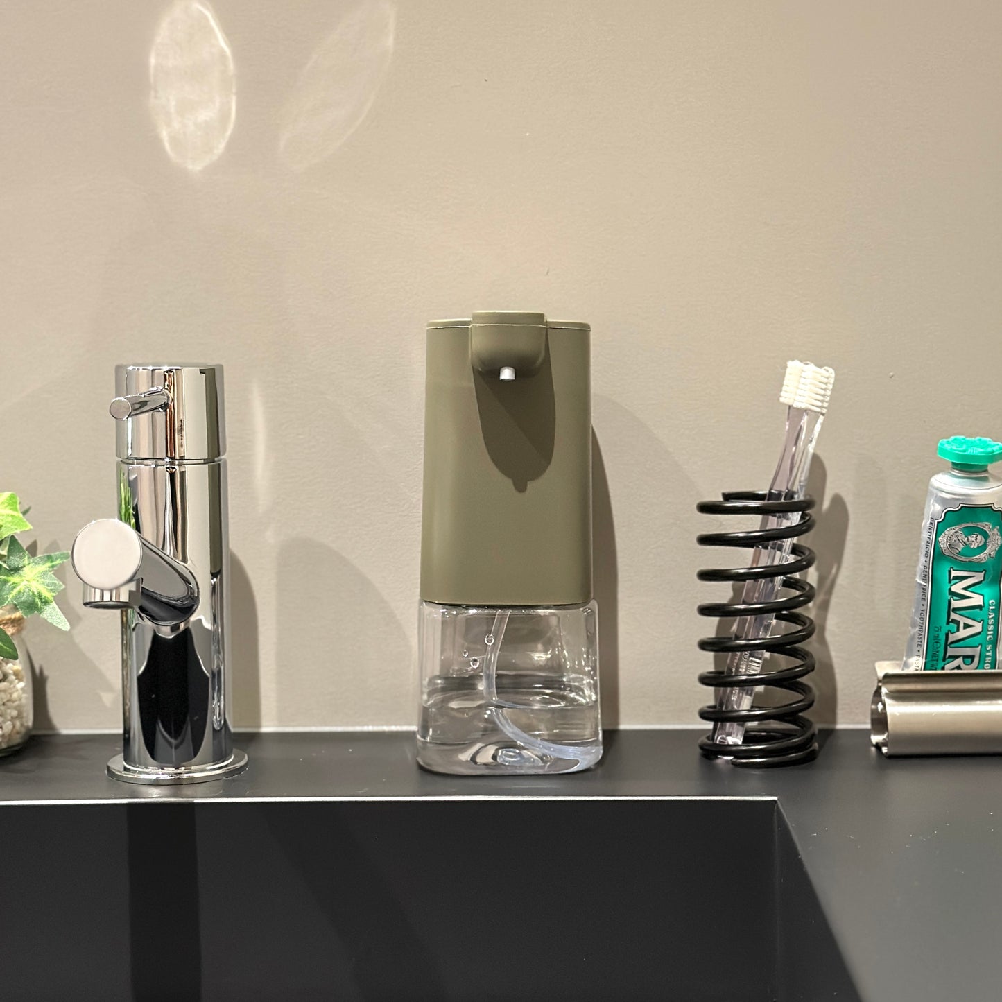 チャコールとクリアの電動泡ソープディスペンサーを洗面台に置いている様子