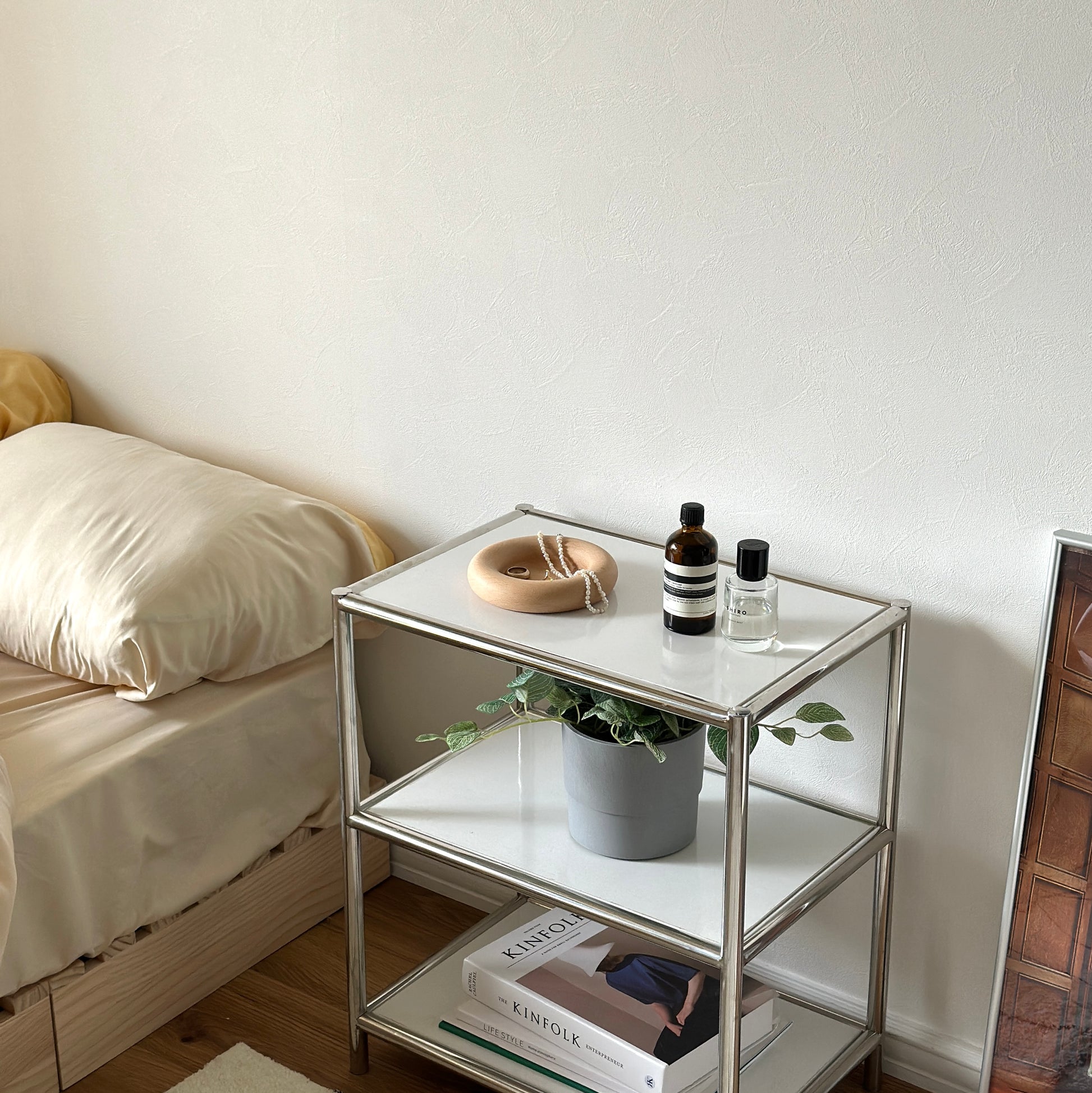 シルバーのフレームの白い3段ラックの一番上にフチがぽってりとした木のプレートが置かれてある。