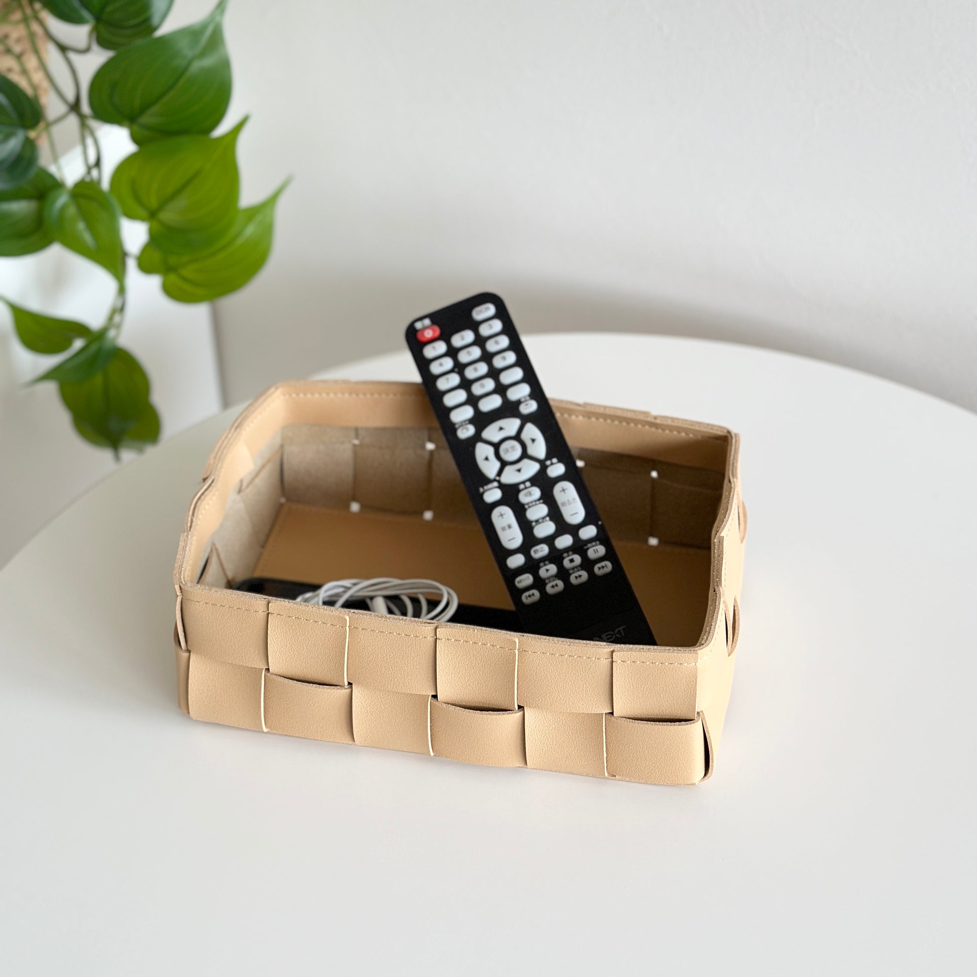 編み込みデザインのキャメルのボックスにテレビのリモコンと充電コードが入っている