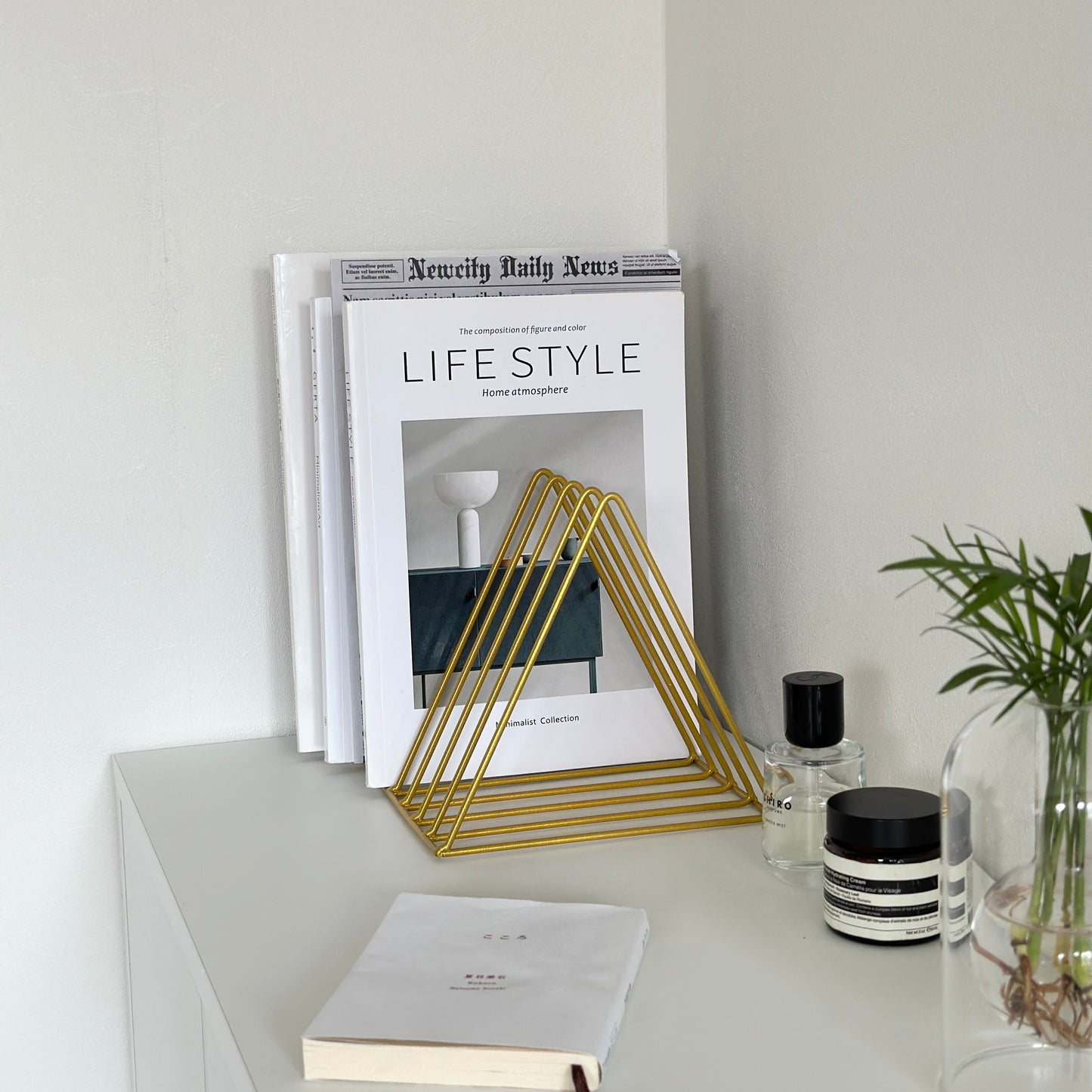 棚の上に置かれて、本や雑誌が飾られたゴールドのアイアンブックスタンド