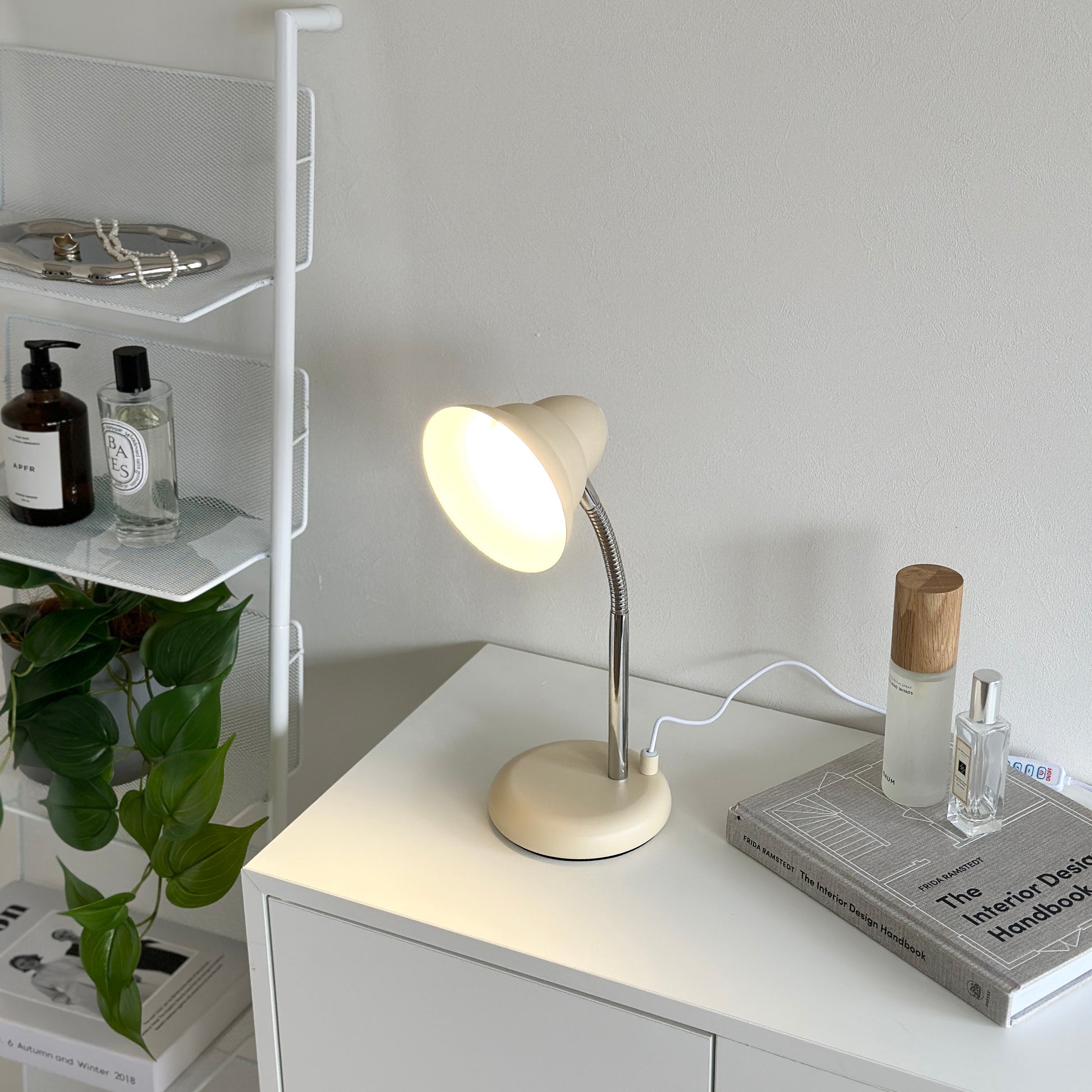 白い棚の上に置かれたくすんだイエローカラーのデスクライトと本の上に置かれた香水が2つ