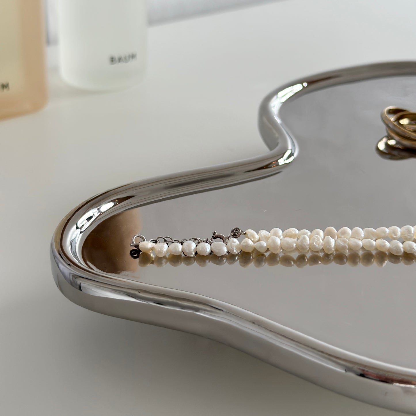 縁がウェーブ状になっている脚付きのシルバープレートの上にアクセサリーが持っている