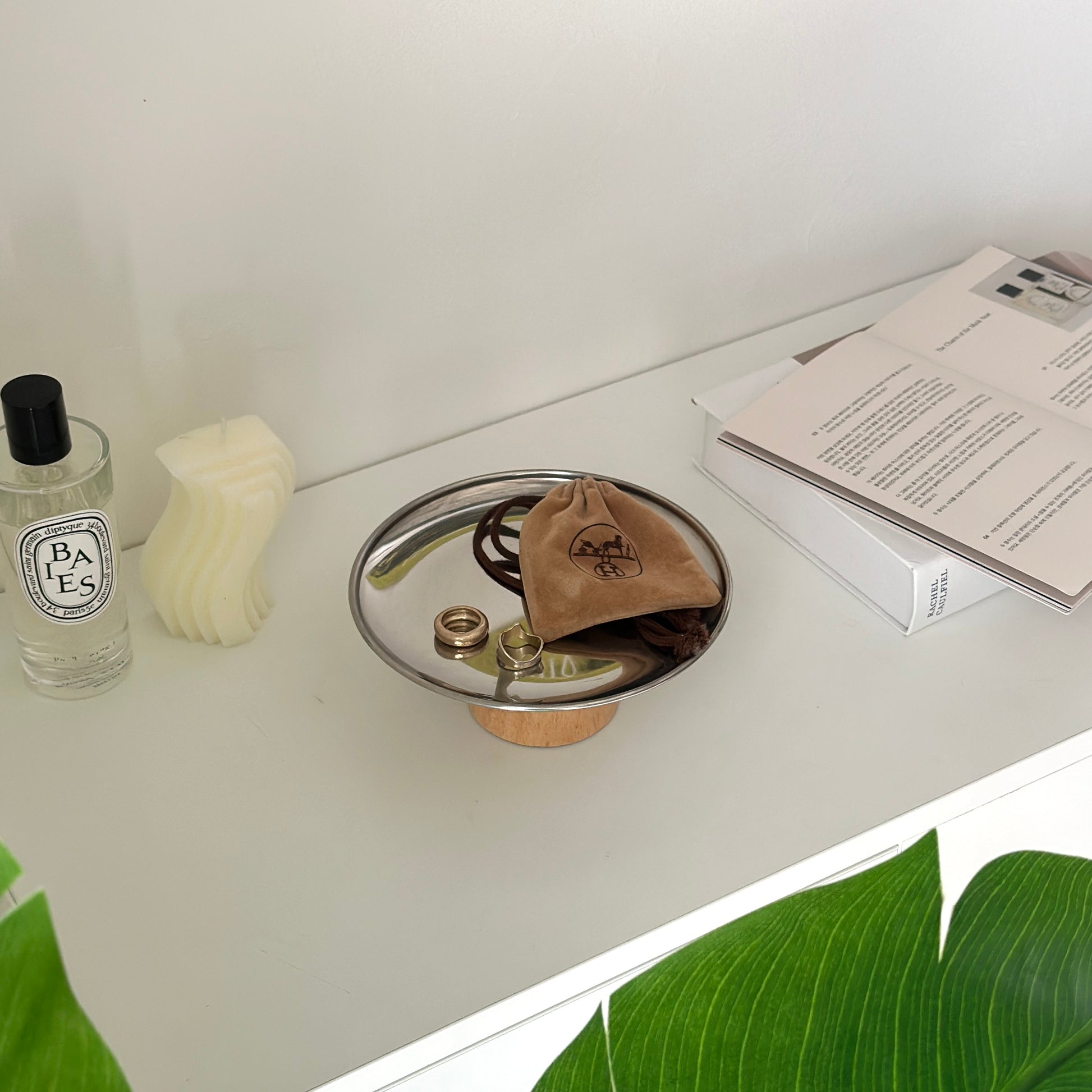 木製の脚とステンレス素材の丸いトレイの上に2つの指輪とポーチが置かれてある。