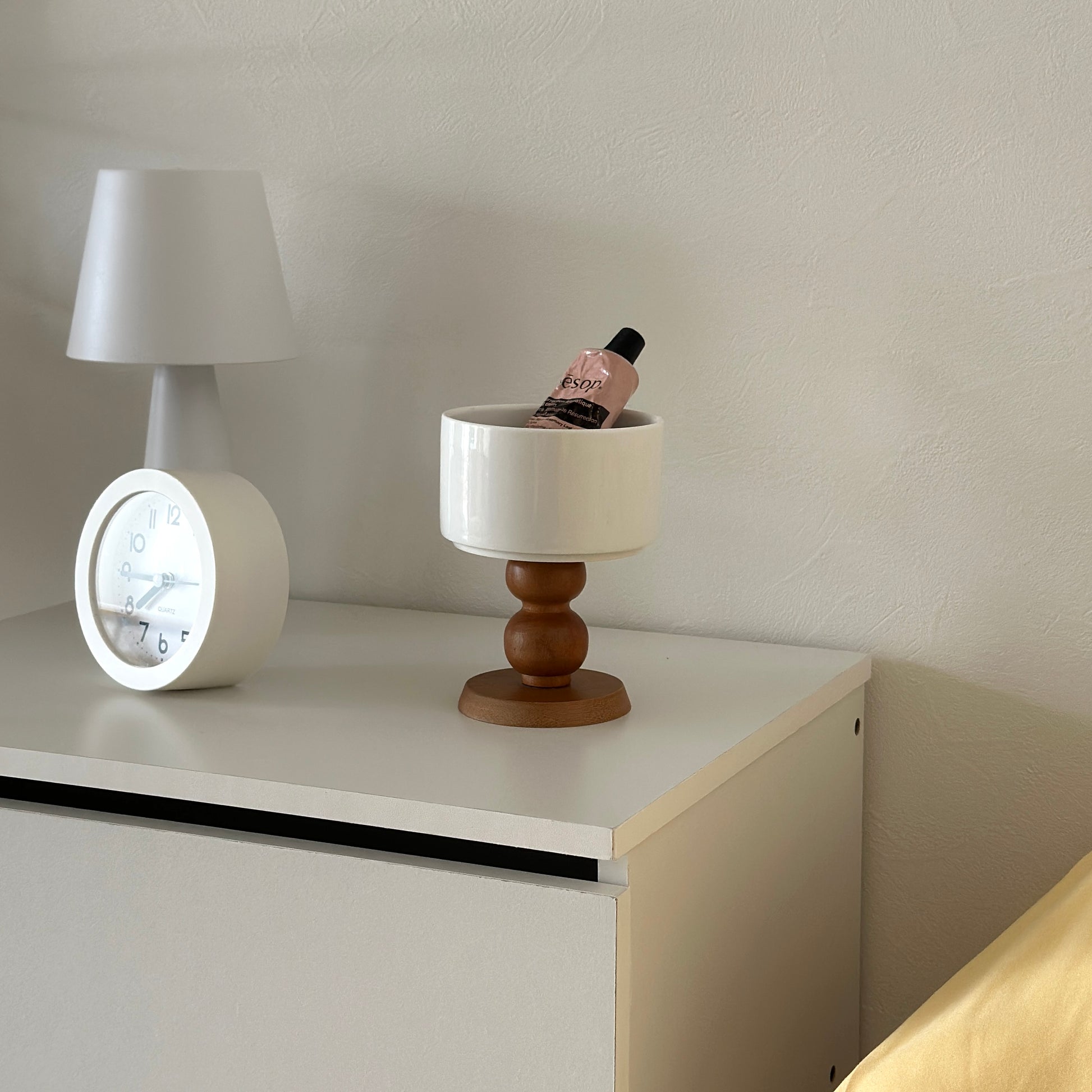 白の棚の上に陶器の器にウッド脚が付いたボウルが置かれてある。