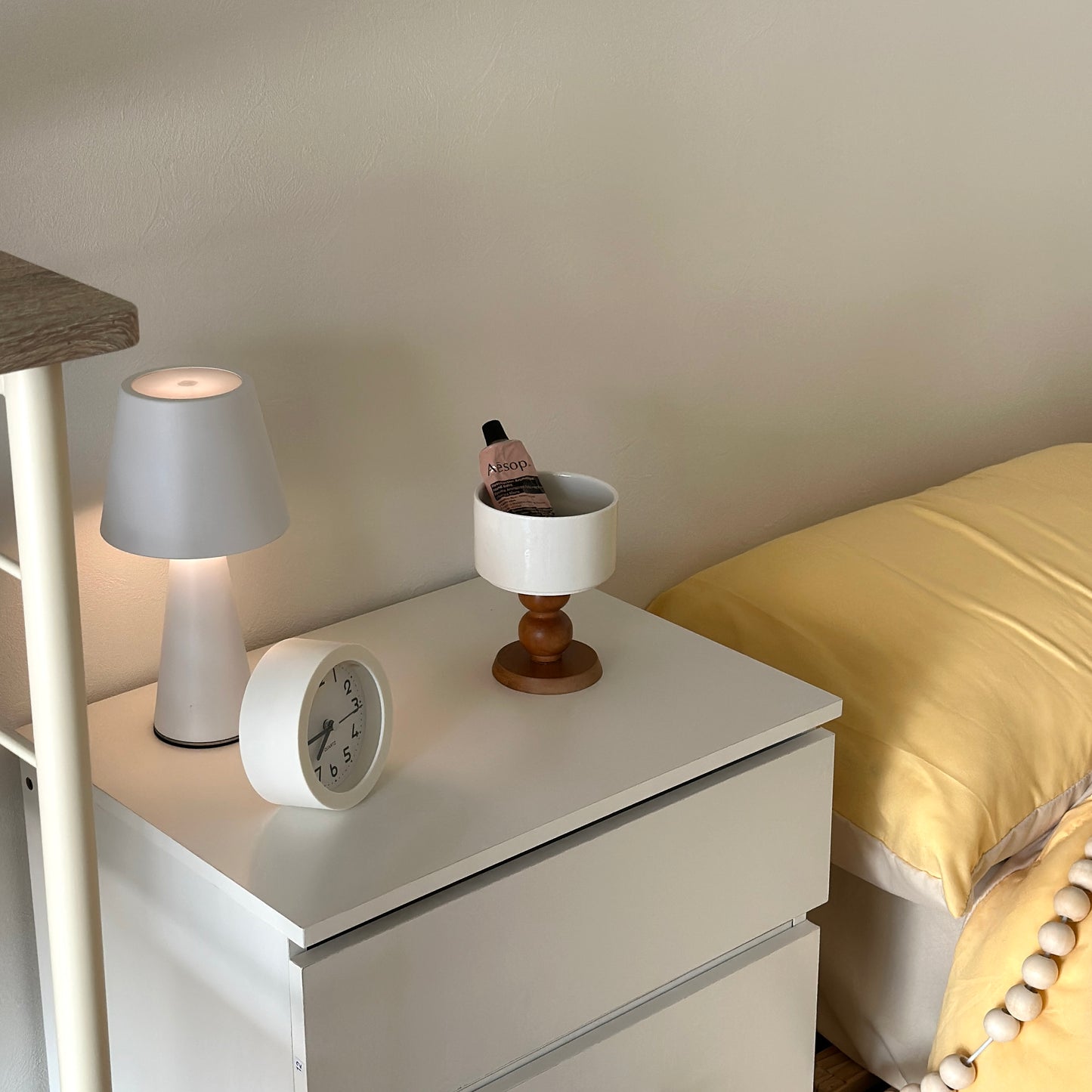 白の棚の上に陶器の器に茶色いウッド脚が付いたボウルが置かれてある。