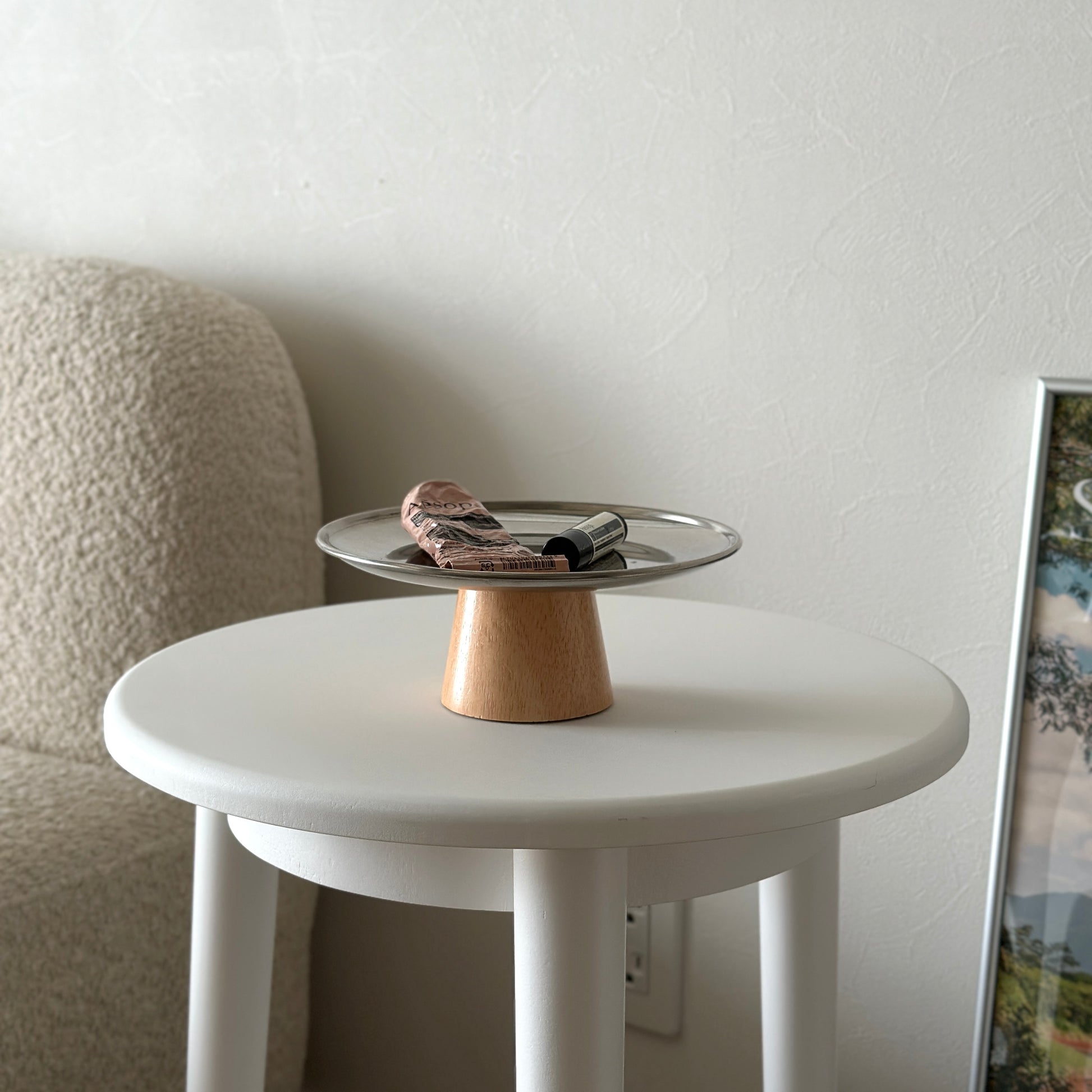 木製の脚とステンレス素材の丸いトレイの上にハンドクリームとリップが置かれてある。