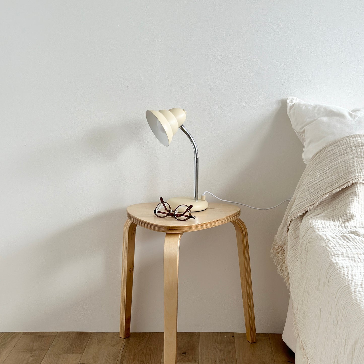 ベッドサイドのテーブルの上に置かれたくすんだイエローカラーのデスクライトとメガネ