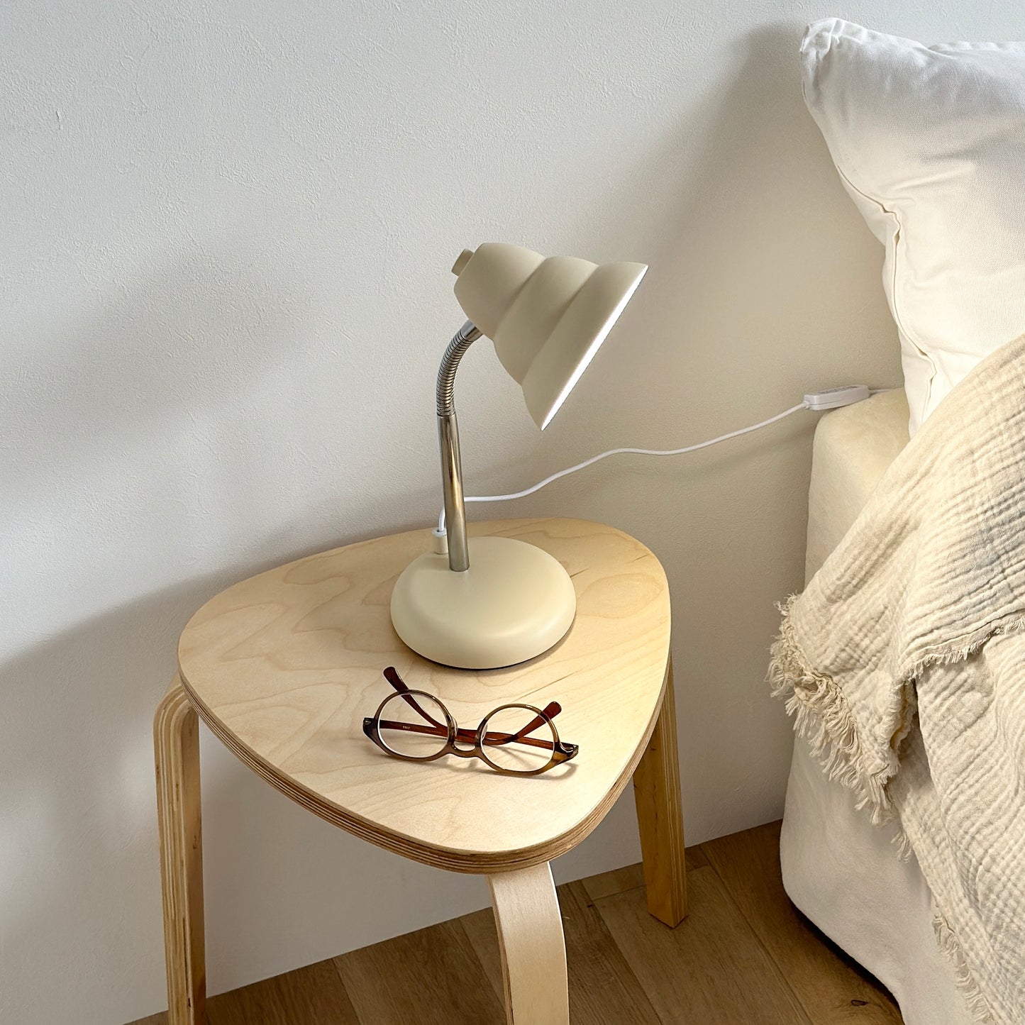 ベッドサイドのテーブルの上に置かれたくすんだイエローカラーのデスクライトとメガネ