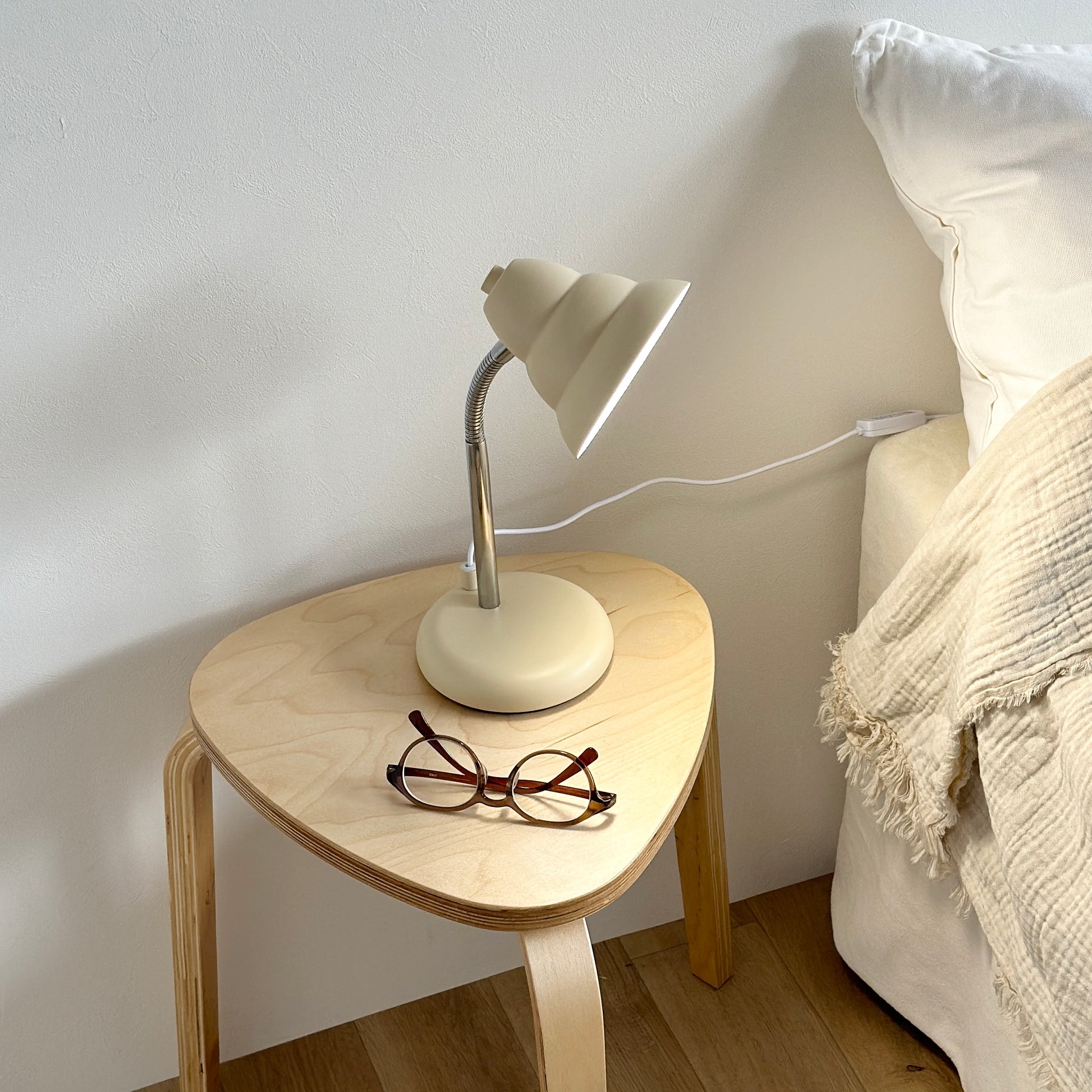 ベッドサイドのテーブルの上に置かれたくすんだイエローカラーのデスクライトとメガネ