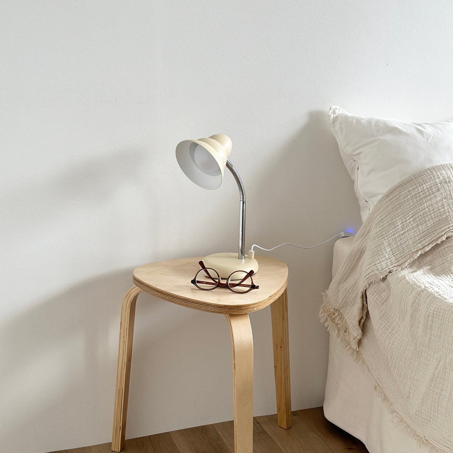 ベッドサイドのテーブルの上に置かれたくすんだイエローカラーのデスクライトとメガネ