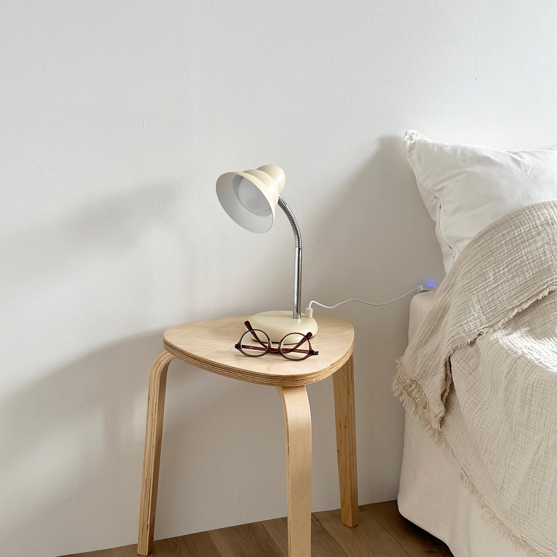 ベッドサイドのテーブルの上に置かれたくすんだイエローカラーのデスクライトとメガネ