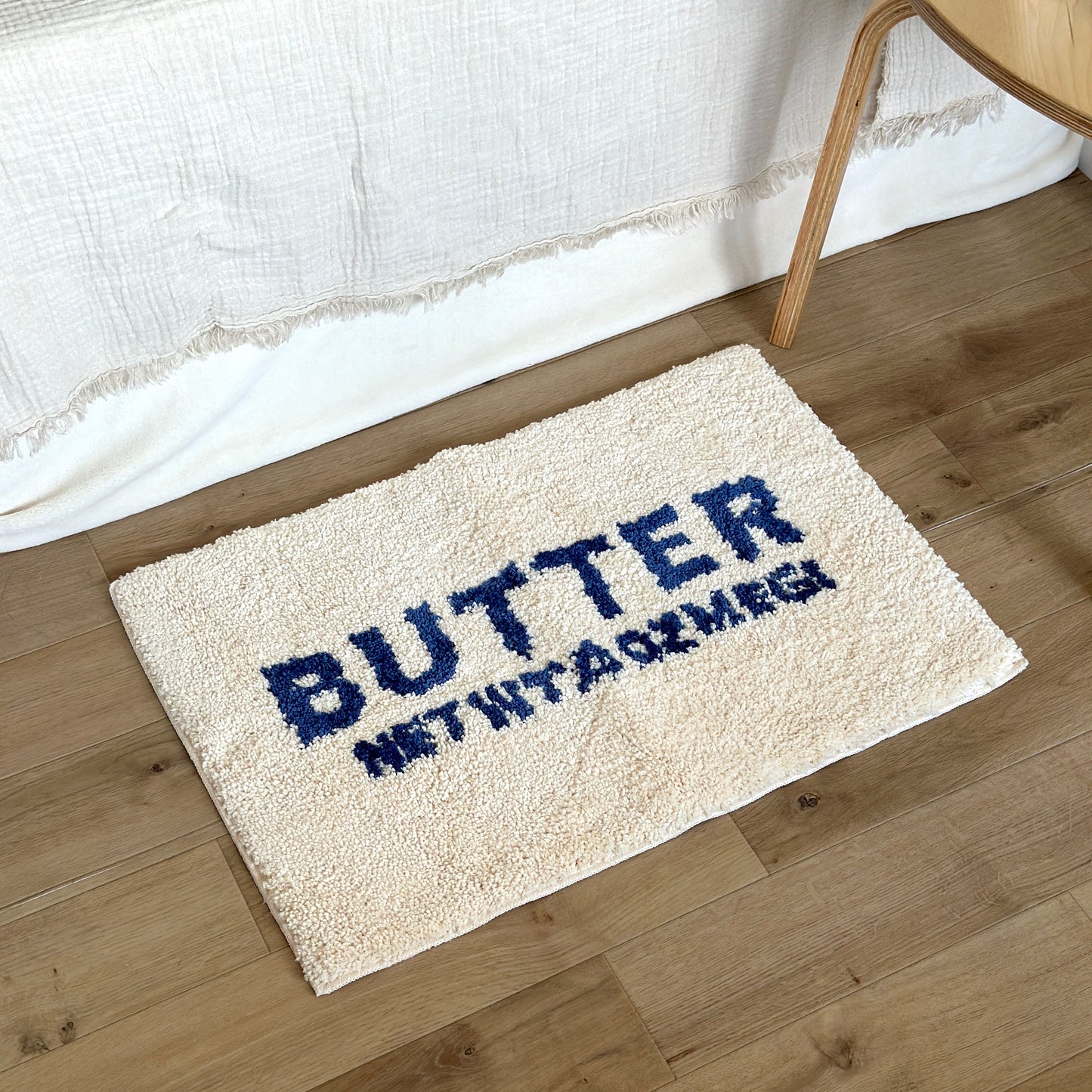 ベッド横に置かれた白地に青文字で”BUTTER”の文字が描かれたミニラグ