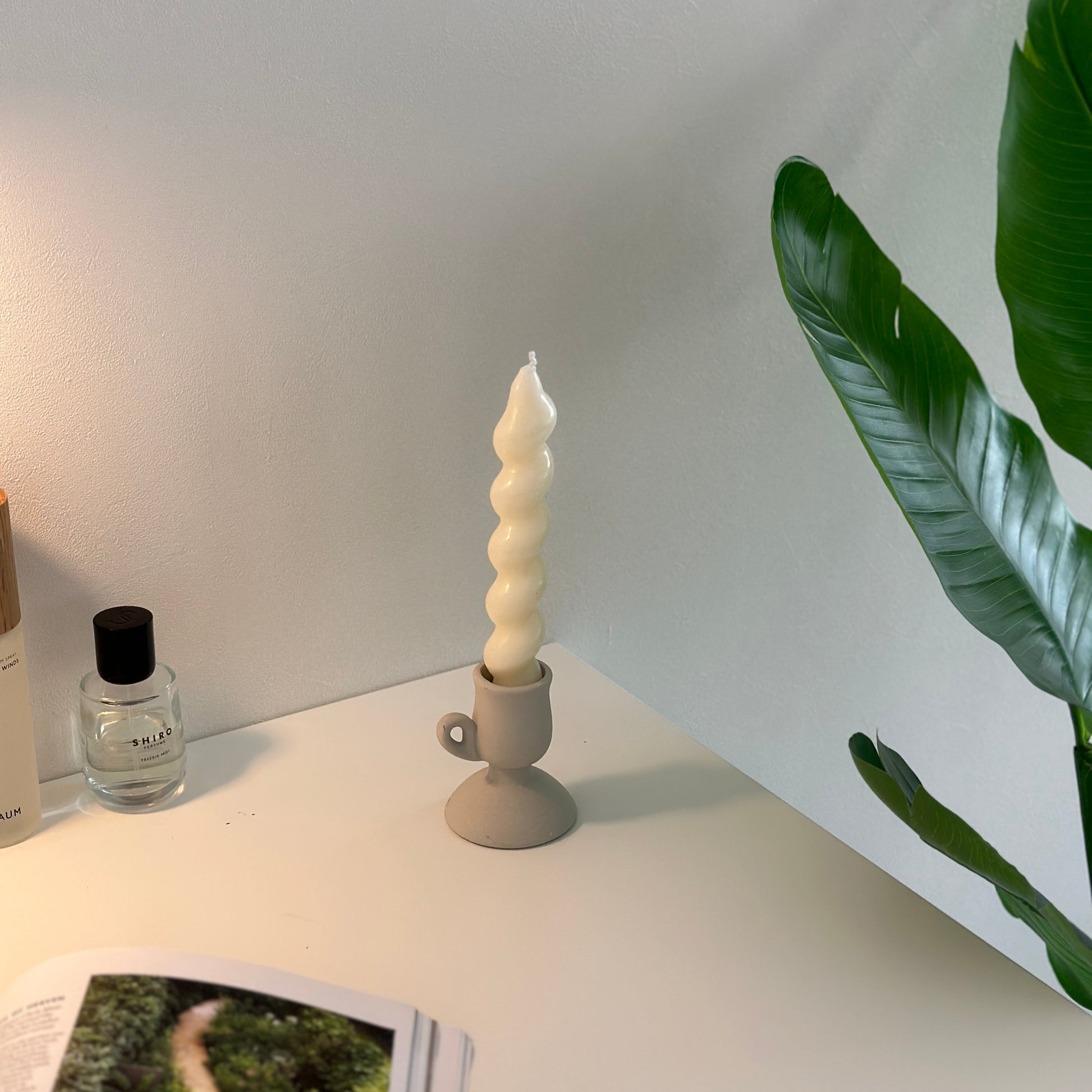 マッドホワイトのキャンドルホルダーにキャンドルがセットされていてその近くに香水や植物が置かれている