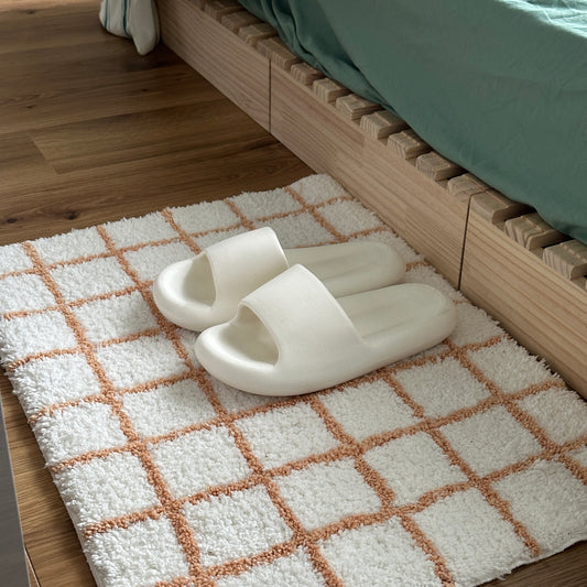 ぽてっとした形の白のスリッパがオレンジと白のチェック柄のミニラグの上に置かれてある