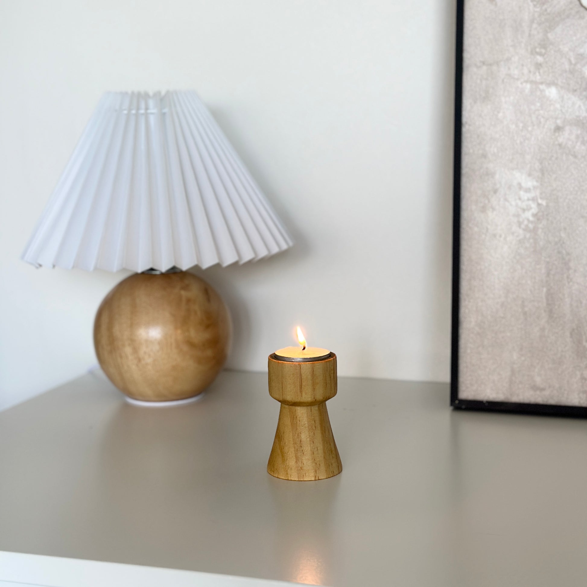 ウッドブラウンの木製のミニキャンドルホルダーとその後ろにライトとアートが飾っている