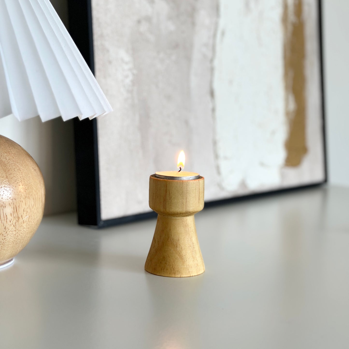 ウッドブラウンの木製のミニキャンドルホルダーと後ろにライトとアートフが写っている写真