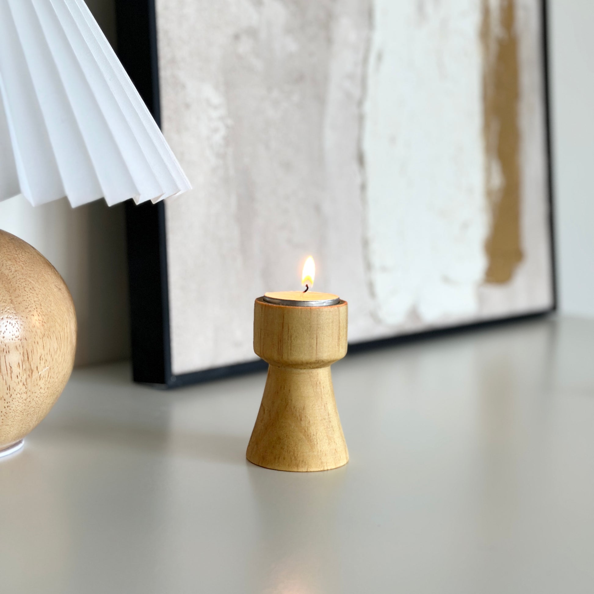 ウッドブラウンの木製のミニキャンドルホルダーと後ろにライトとアートフが写っている写真