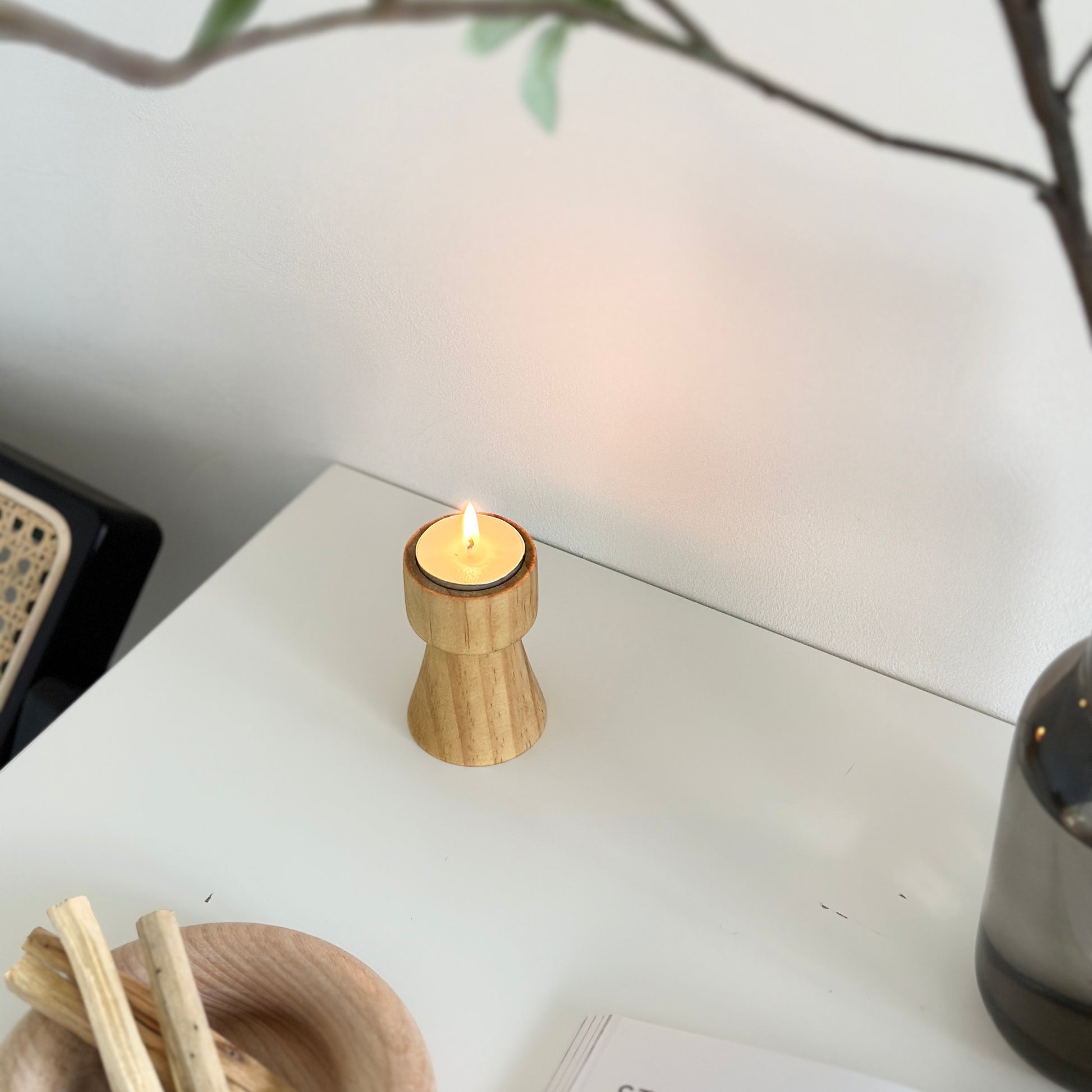 ウッドブラウンの木製のミニキャンドルホルダーを上から映し、植物や木製のプレートが写り込んでいる写真