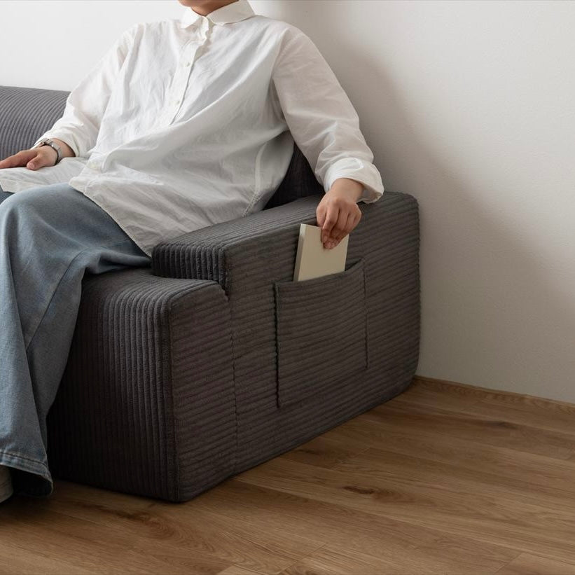 Dark gray corduroy two-seater rib design low sofa with built-in pocket holding a book