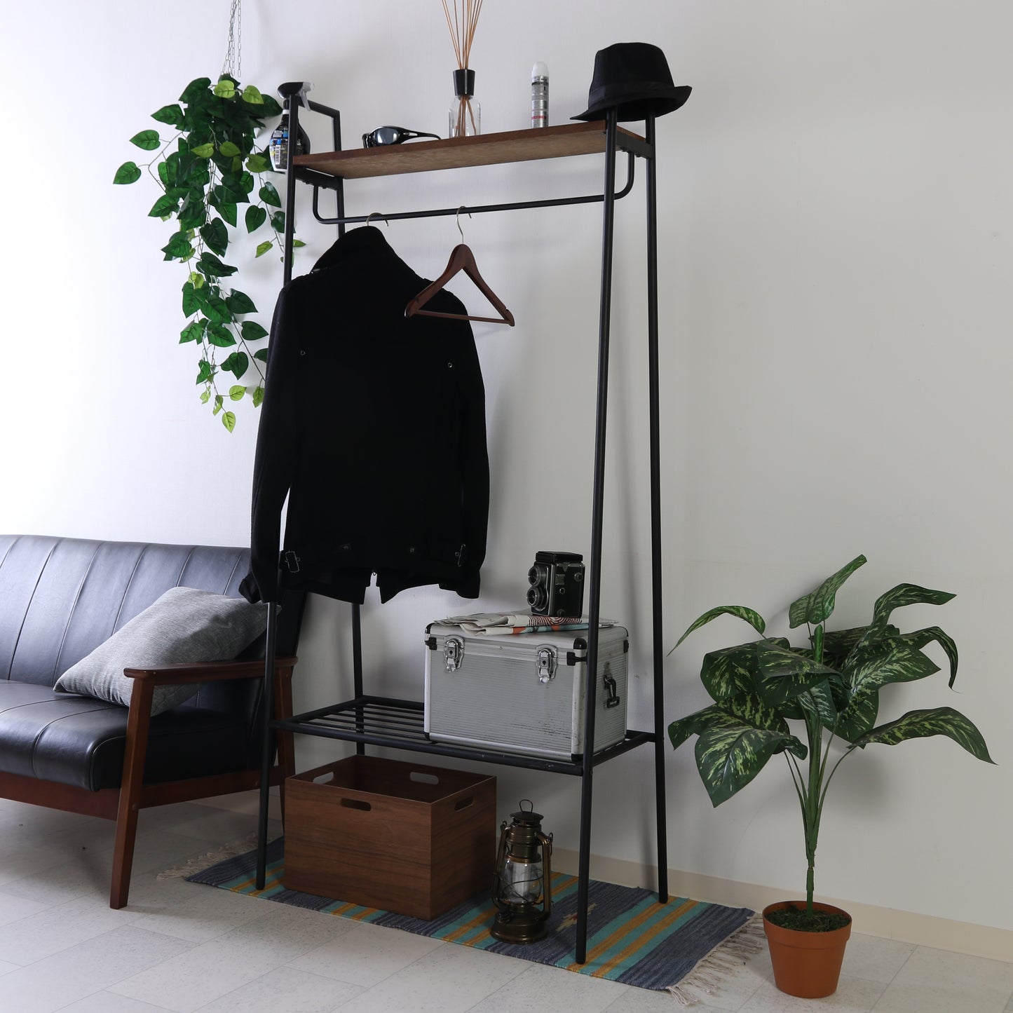 黒の金属と木製のウッドラック付きハンガーラックにサングラス、帽子、装飾品が置かれた上棚付き