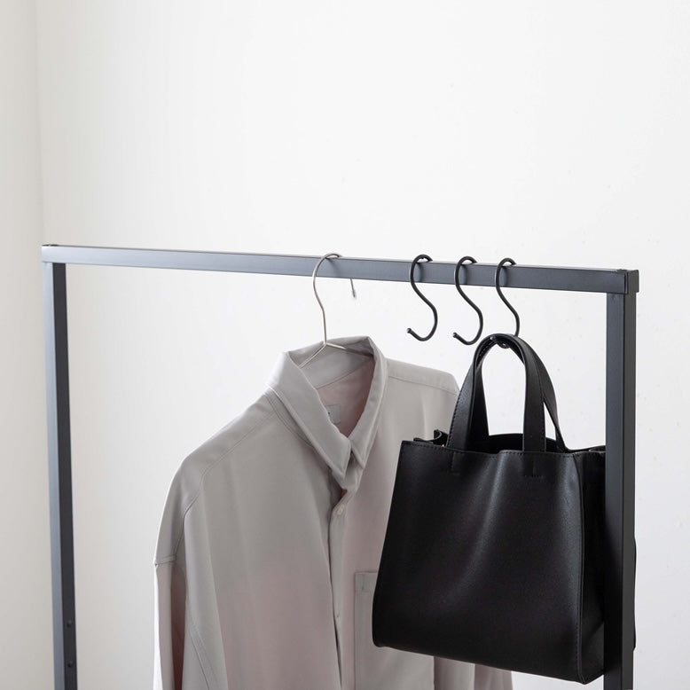 シンプルなブラックのスチール素材のハンガーラックに洋服やカバンがかけられている様子