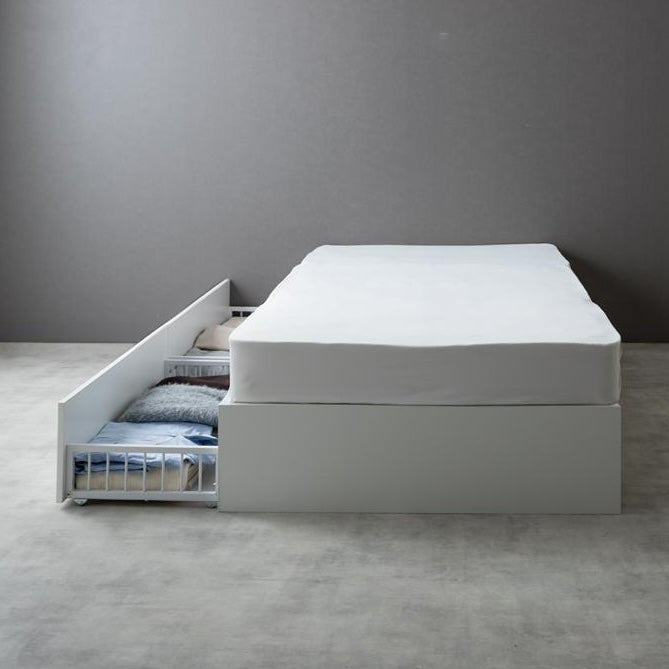 シンプルな白のベッドフレームの向かって左側に引き出しを設置して使っている様子