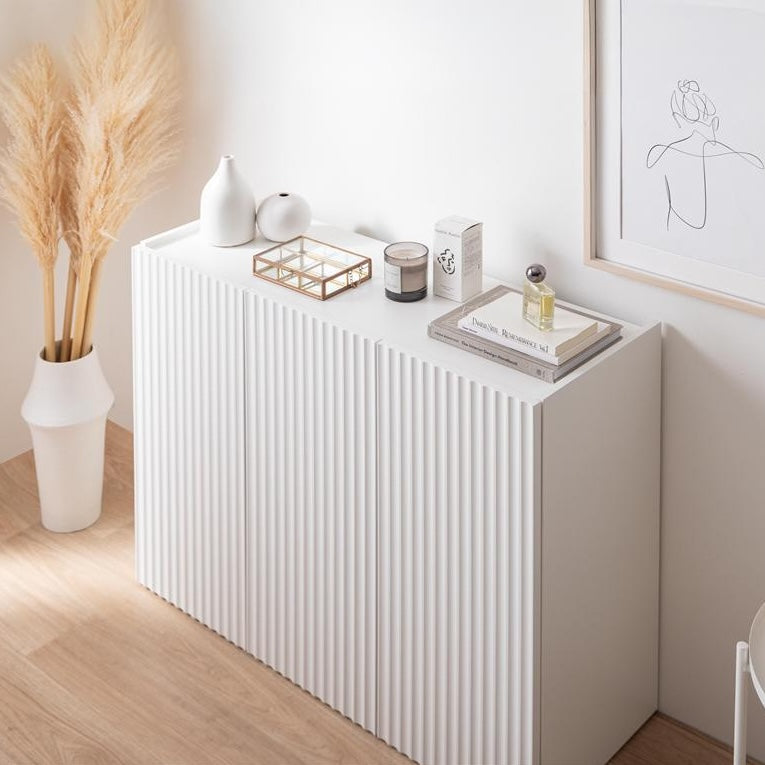 波型扉のホワイトのキャビネットの上に白い花瓶やアクセサリー、香水、本が置かれてある様子