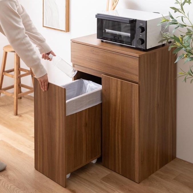 ブラウンのゴミ箱とキッチンボードが一体となった収納家具のゴミ箱を引き出してゴミを捨てている様子