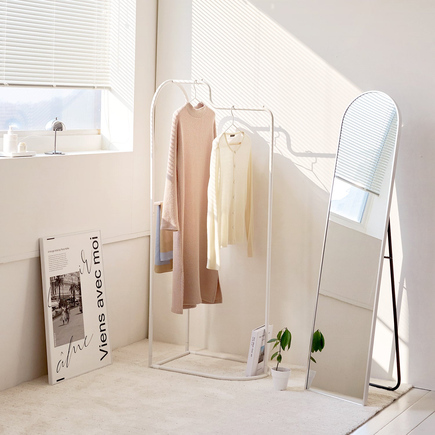 Roomnhomeの白い金属製アーチカーブハンガーに2着の服がかかり、近くに曲面鏡があります。