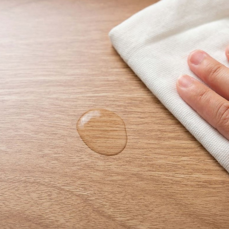 ナチュラルウッドカラーの4つの収納スペースが付いたサイドテーブルにもなる収納ワゴンの天板にこぼれた水滴を布でふきとる様子