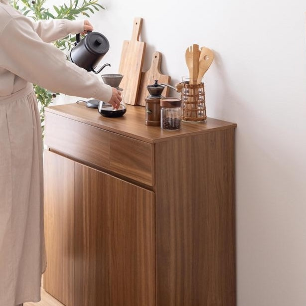 ブラウンのゴミ箱とキッチンボードが一体となった収納家具の天板でコーヒーを淹れている様子