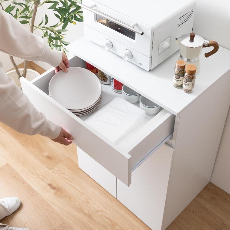 ホワイトのゴミ箱とキッチンボードが一体となった収納家具の引き出し収納部分を開けてお皿を収納している様子