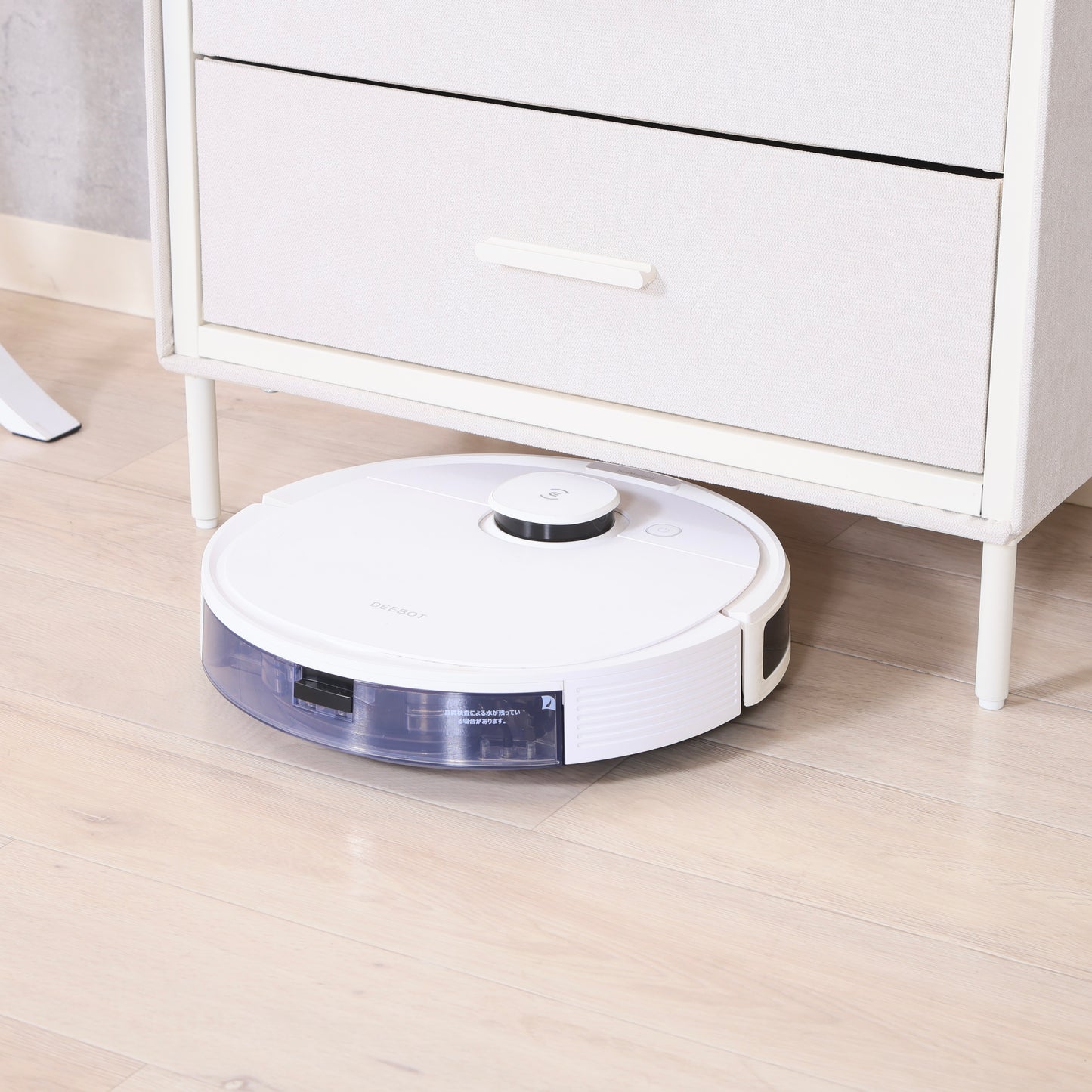 ファブリック素材の収納チェストの脚元スペースにロボット掃除機が通っている様子