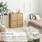 白い部屋に置かれた低い木目調キャビネット、観葉植物、ソファ、ベッド、コーヒーテーブル。