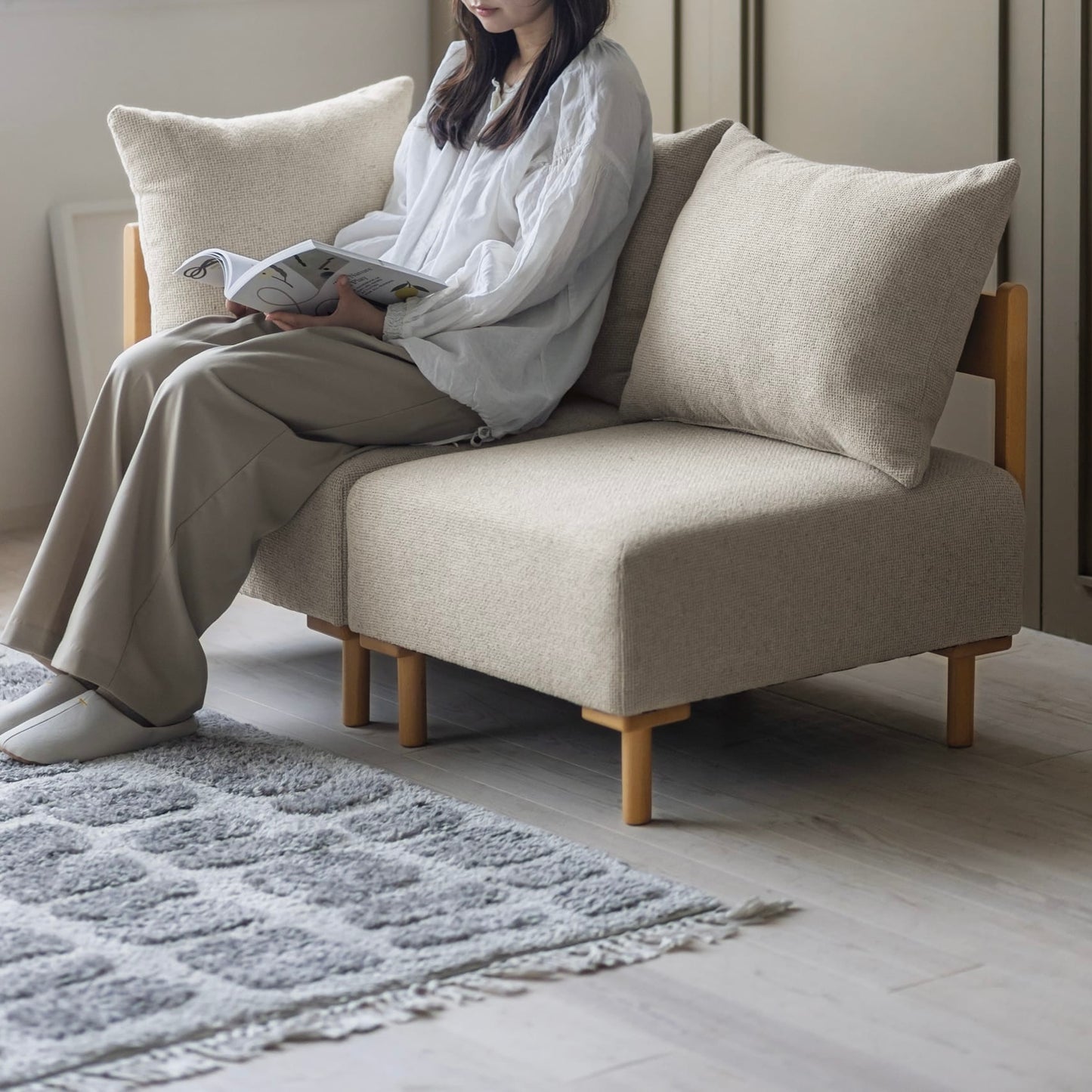 木製フレームのベージュのソファに人が座っている様子