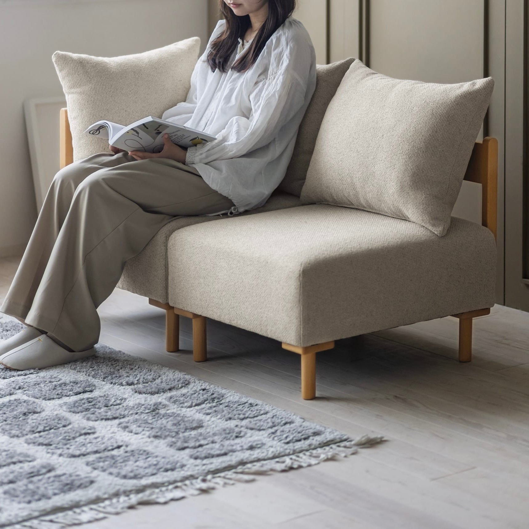 木製フレームのベージュのソファに人が座っている様子