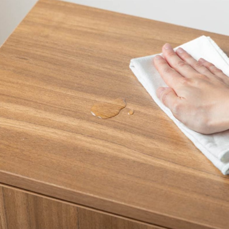 ブラウンの脚付きマルチキャビネットの天板に溢れた水を拭き取ろうとしている様子