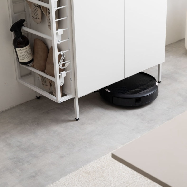 ホワイトのラック付きキャビネットの下に掃除ロボットが入っている様子