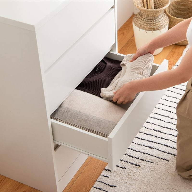 白の引き出しが4段のチェストの引き出しを開けて洋服をしまっている様子