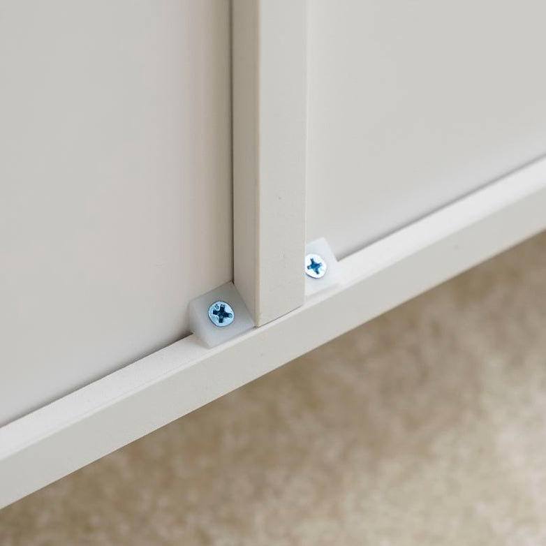 白の扉付きの収納とオープン棚が組み合わさったキャビネットの背面を横揺れ防止ネジで固定している様子