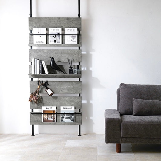 グレーの突っ張りディスプレイラックをソファ横に設置している様子