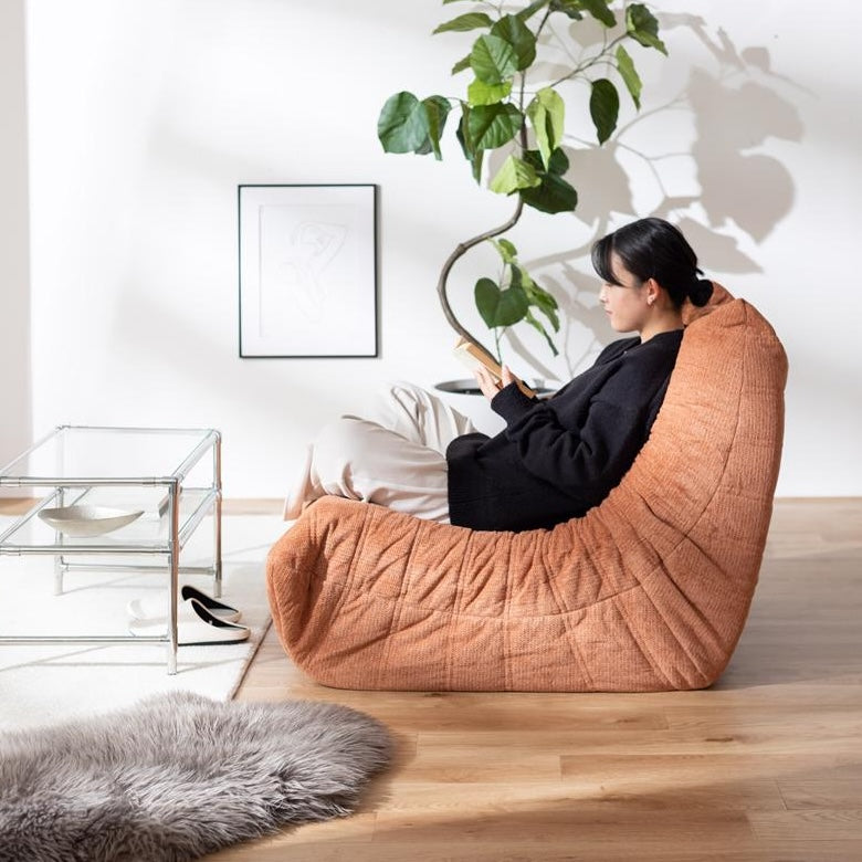 曲線フォルムと低重心デザインがお洒落なオレンジ色の1人掛けソファが部屋に置いてあるインテリア