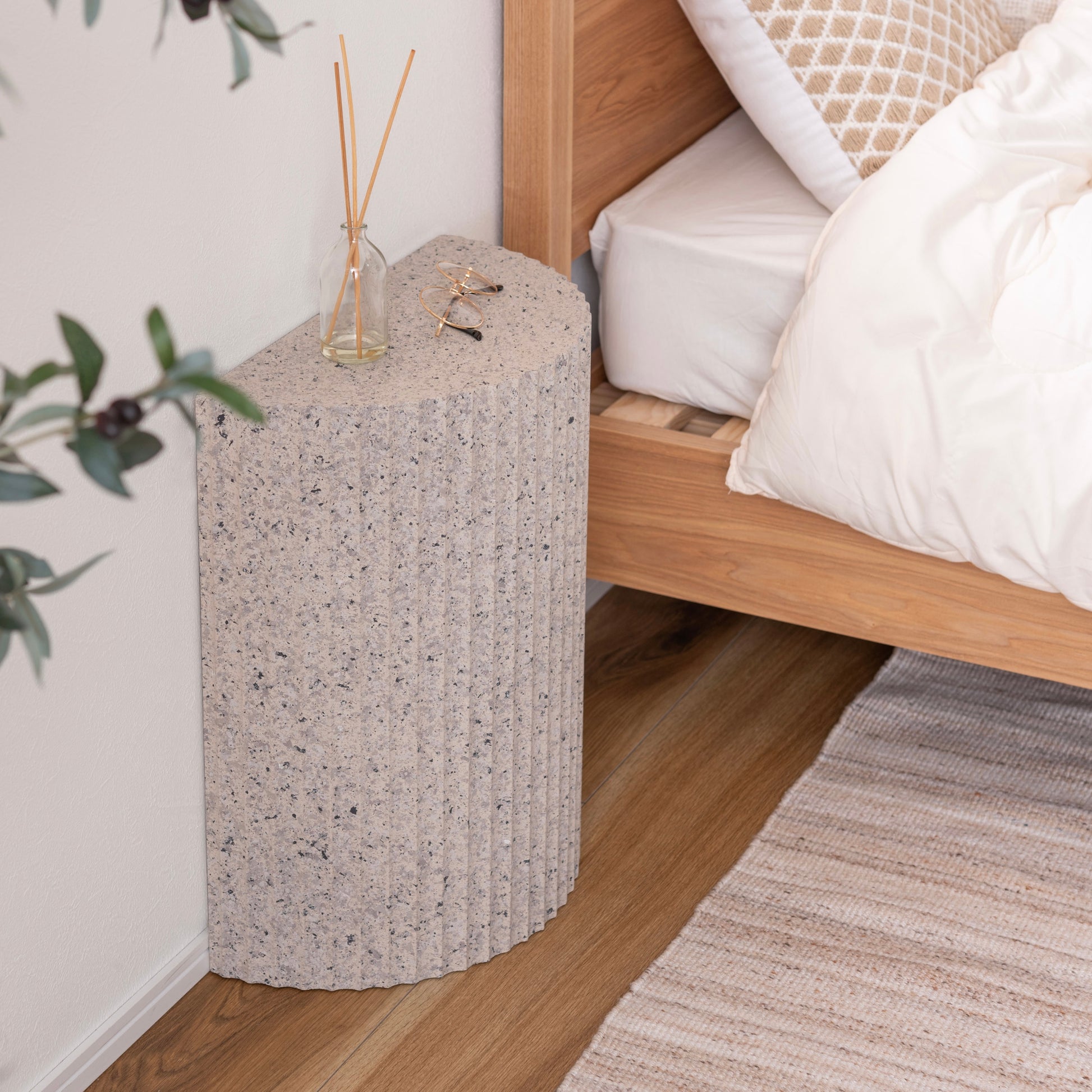 テラゾー柄の半円のスツールがベッドサイドに置かれている様子