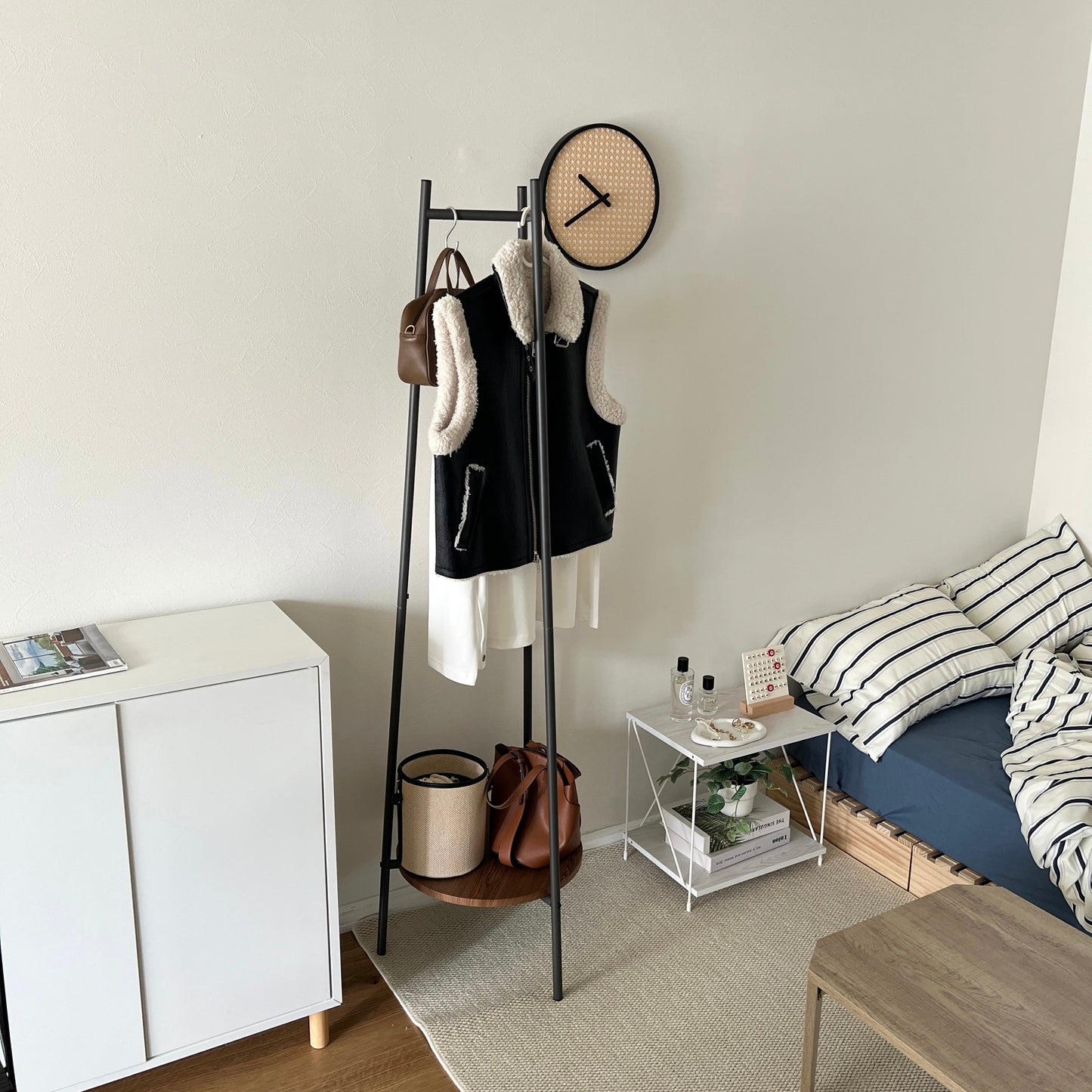 部屋の中で黒いコンパクトでスタイリッシュなハンガーラックに洋服がかかっている様子