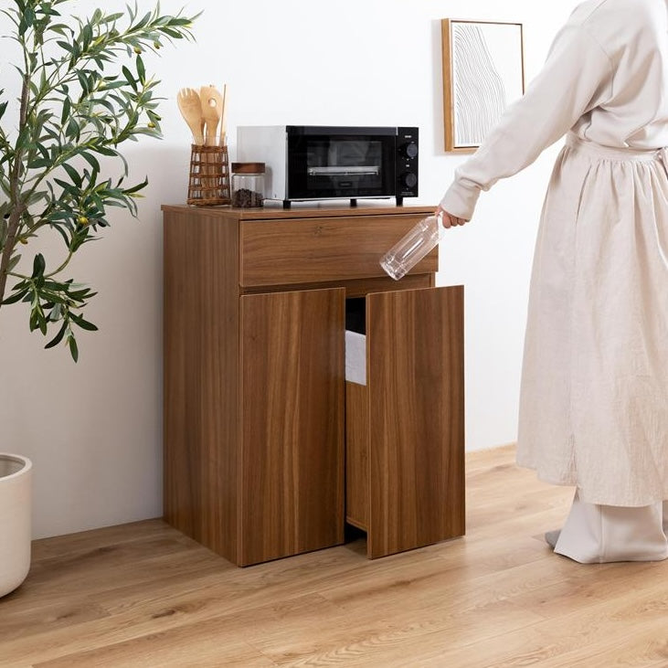 ブラウンのゴミ箱とキッチンボードが一体となった収納家具のゴミ箱を引き出してゴミを捨てている様子