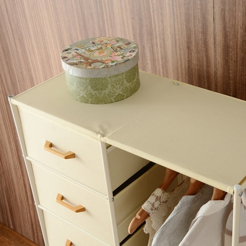 アイボリーの衣類を掛けるハンガーポールと7杯の引き出しを組み合わせた多機能なハンガーラックの上に箱を置いている様子